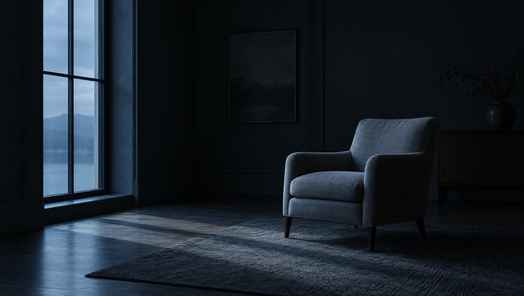 An empty upholstered armchair in a dim, quiet room, cool light from a tall window falling across the floor.