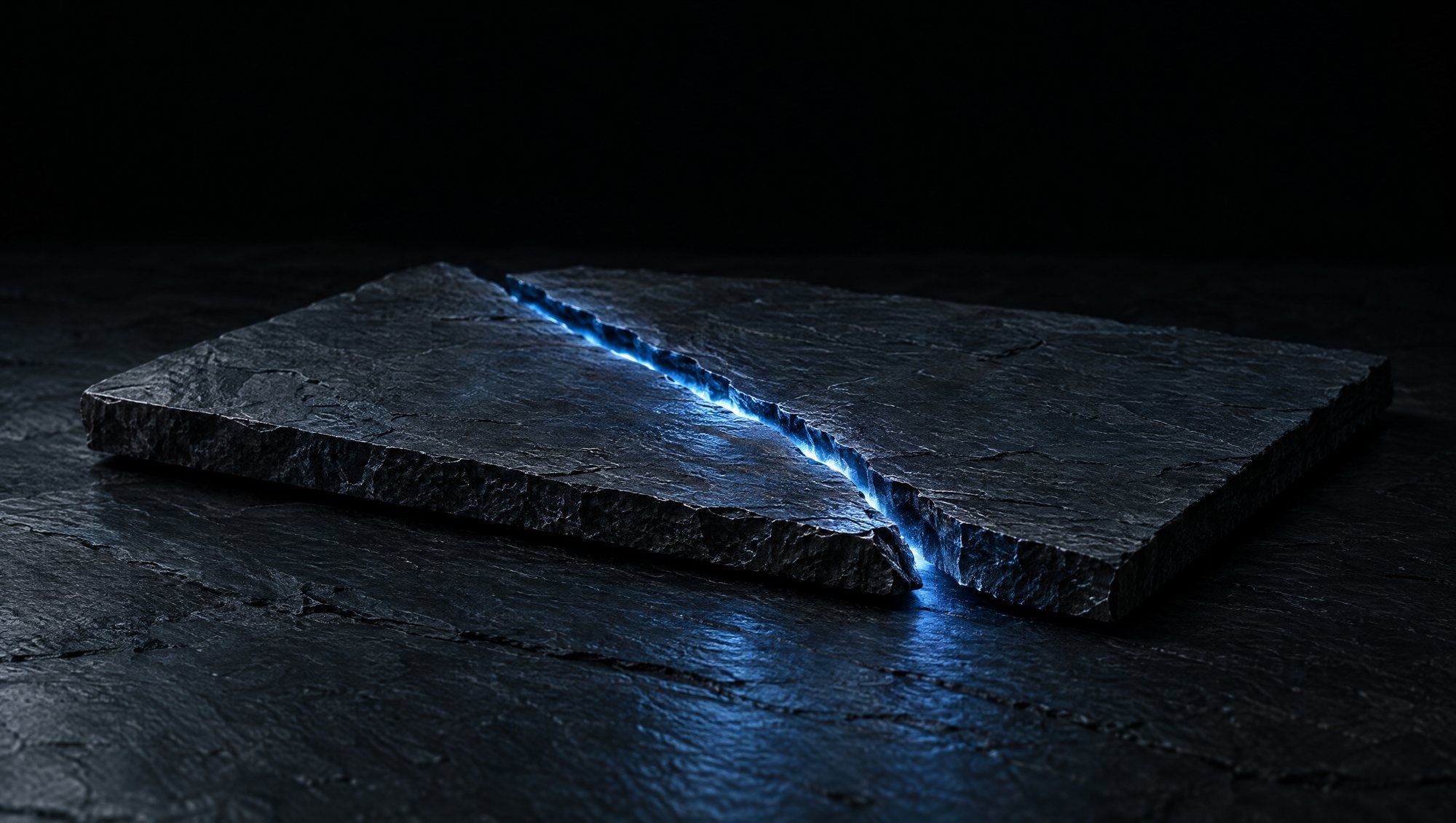 A flat tile of dark slate split diagonally by a single crack, a thin line of cool slate-blue light glowing through the seam, resting on dark slate against a black background.