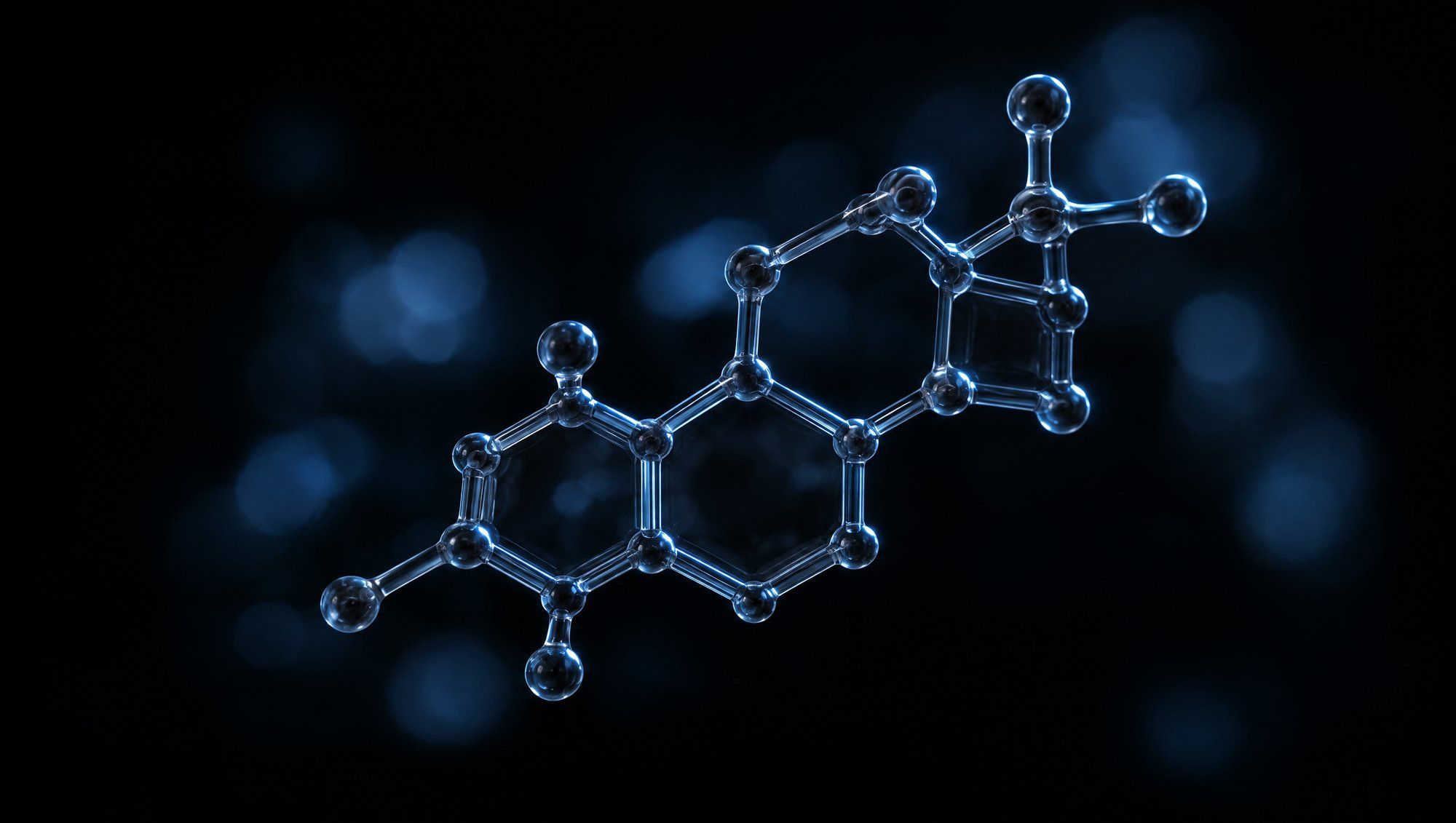 A smoky glass model of a molecule built from joined rings, floating against black with slate-blue edge light and soft blue bokeh.