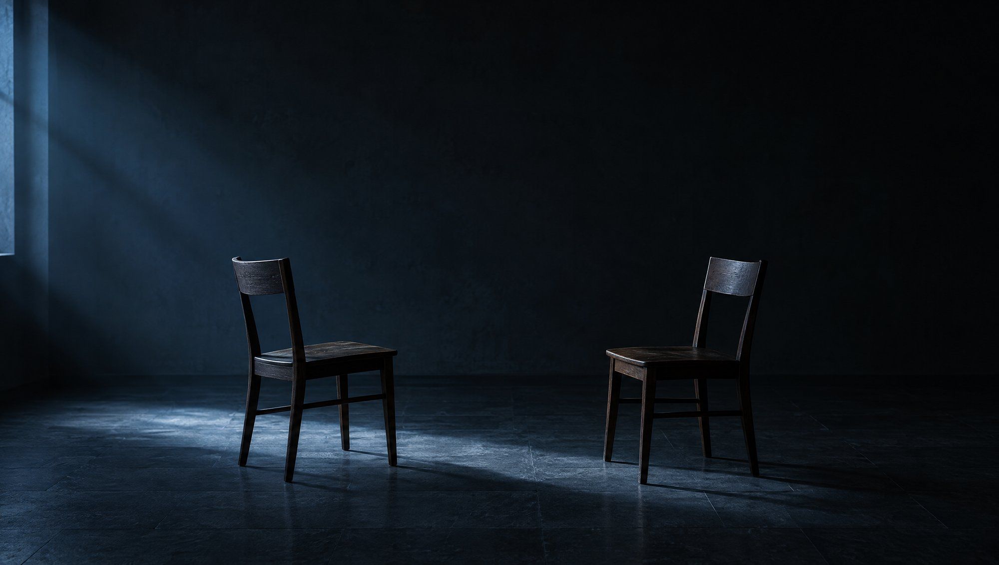 Two empty dark wooden chairs facing each other in a dim room with a dark stone floor, a band of cool slate-blue window light falling across the floor between them.
