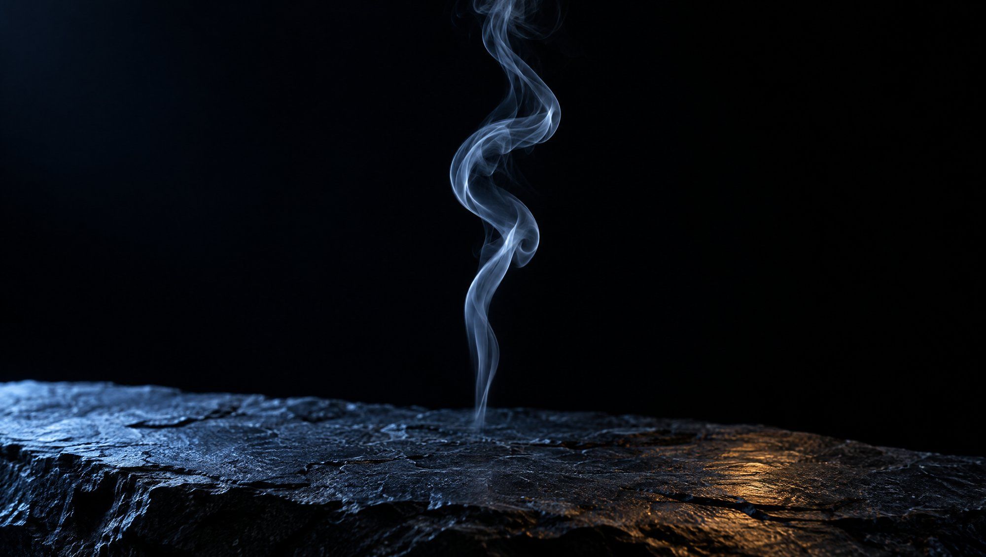 A single thin wisp of pale smoke curling upward above rough dark slate stone against black, edge-lit in cool slate-blue light with a faint amber reflection on the stone.